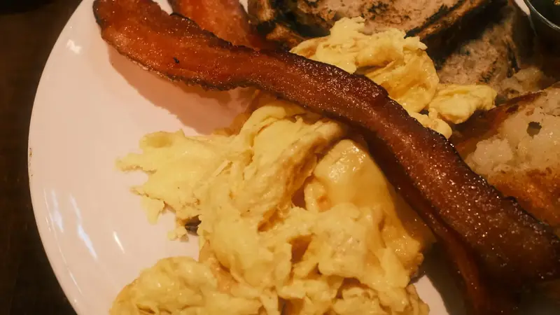 Breakfast plate with scrambled eggs, crispy bacon strips and grilled toast