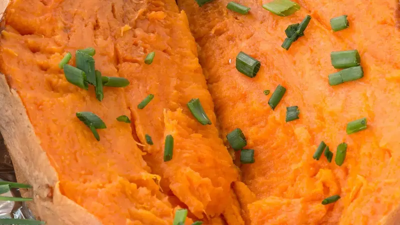 Whole baked sweet potato split open with soft orange flesh and chopped chives
