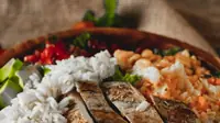 Sliced cooked chicken breast served with rice and salad in a bowl