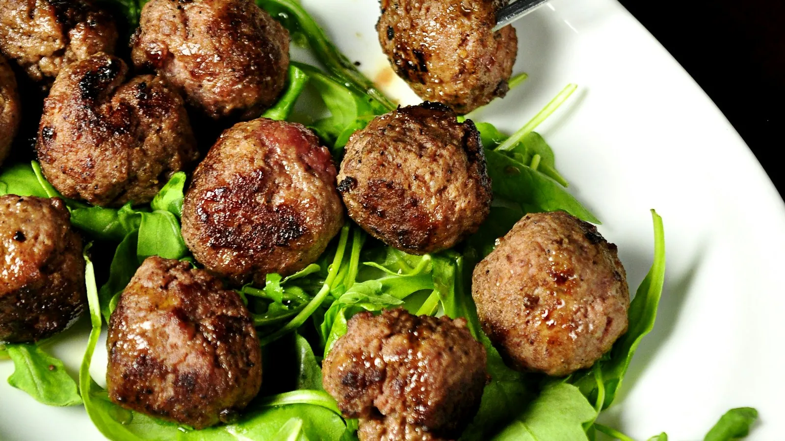 Cooked browned meatballs arranged on an oval white plate
