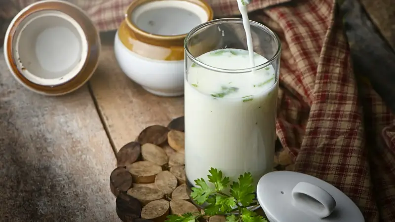 A clear glass of milk beside green leaves and a small dish of cream