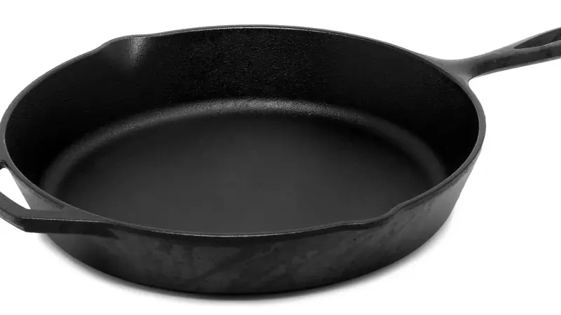 A bare black cast iron skillet with a long handle on a plain white background