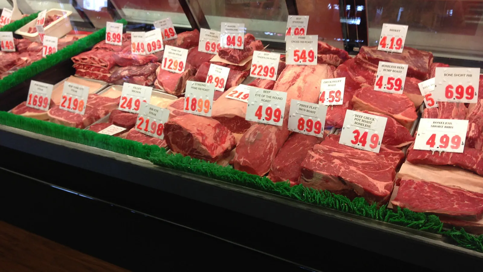 A grocery store meat case full of beef roasts and steaks with red price tags