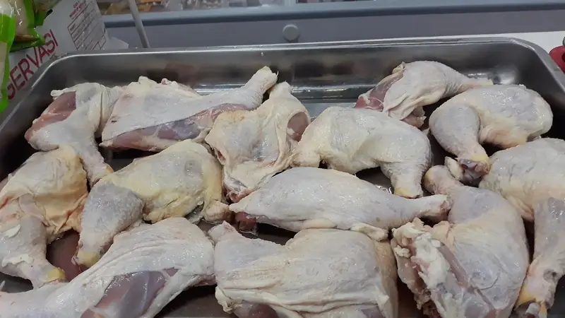 Raw chicken leg quarters with pale yellow skin laid out in a steel tray at a store counter