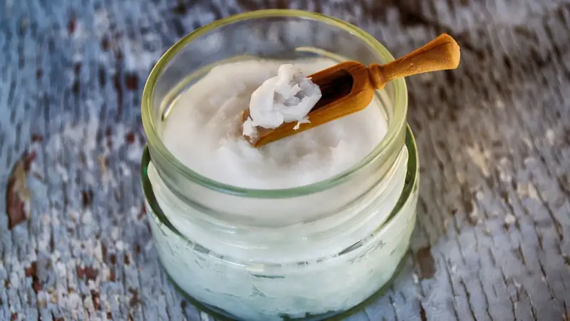 Glass jar of solid white coconut oil with a wooden spoon