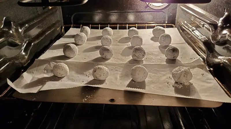 Hand sliding a baking sheet of chocolate crinkle cookies into a hot home oven