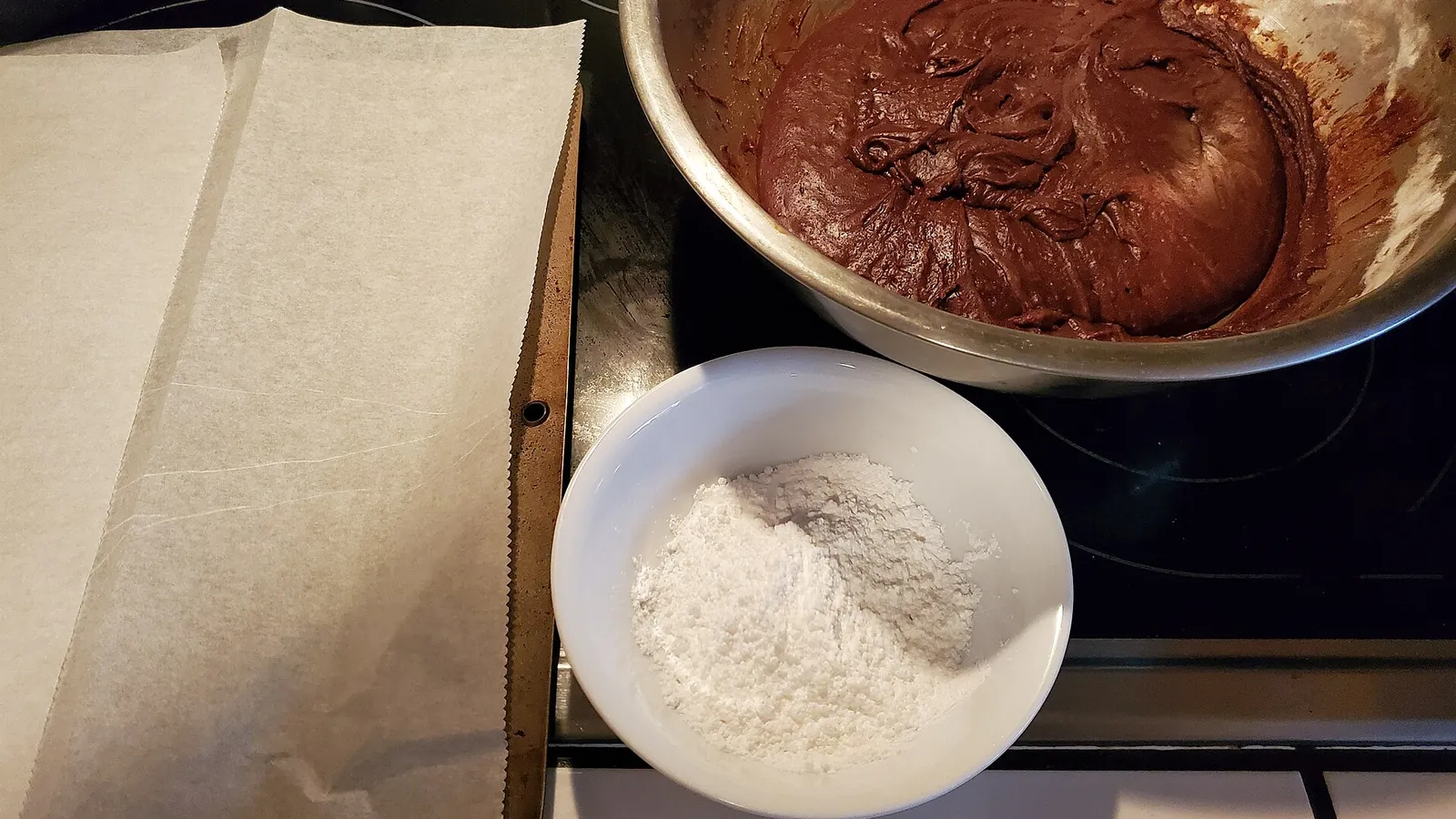 Chilled chocolate crinkle cookie dough beside powdered sugar and a lined baking sheet