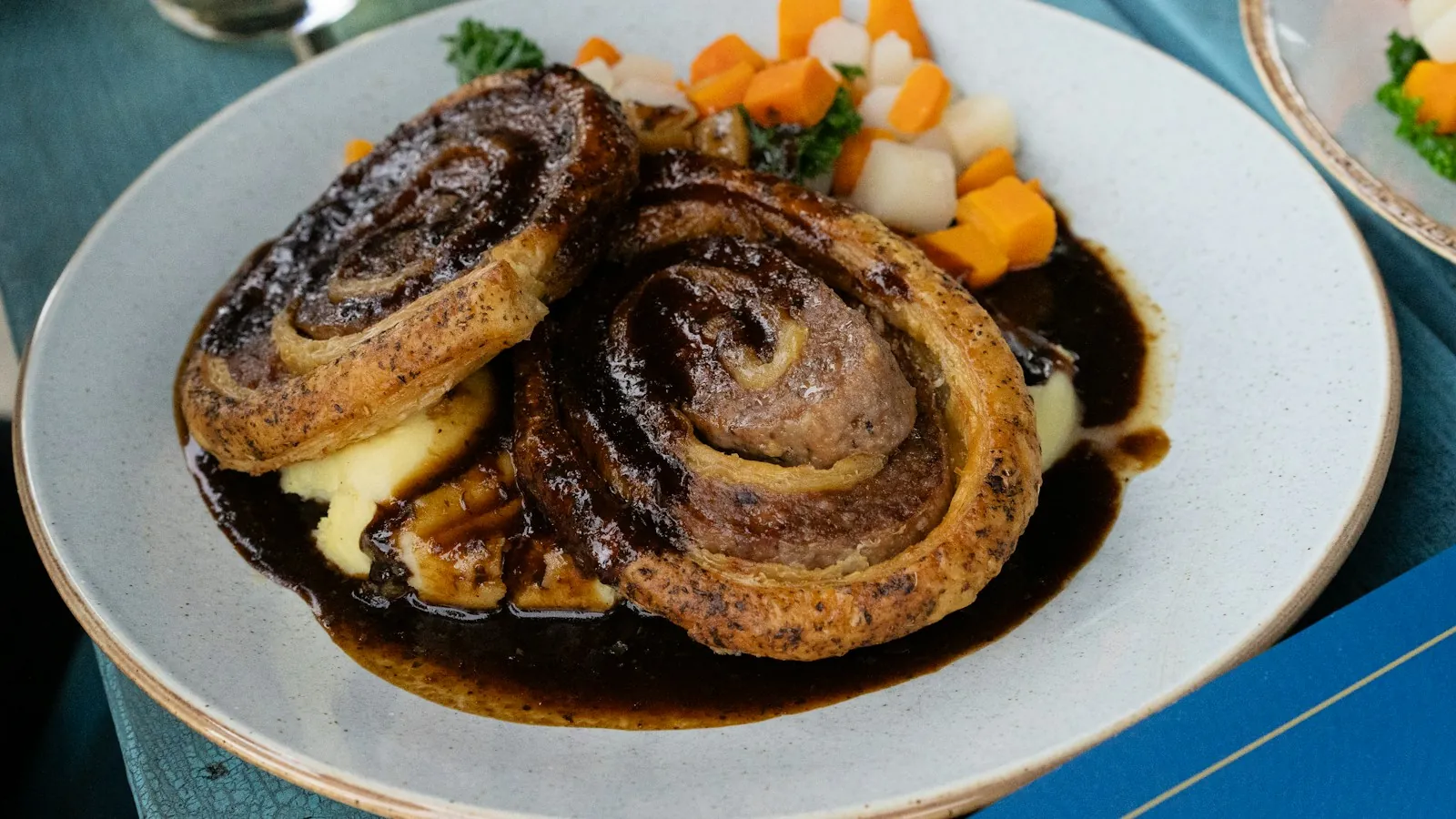 Sliced beef with carrots on a plate covered in glossy brown gravy