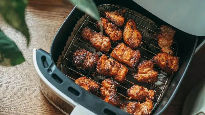 Crispy chicken pieces cooking in the basket of a modern air fryer