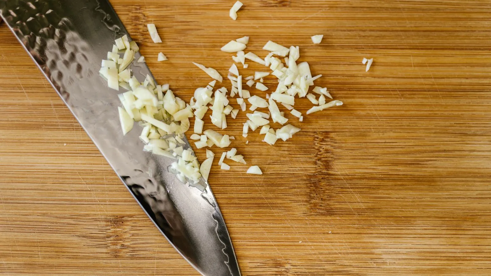 Chopped garlic on a wooden cutting board beside a stainless steel knife