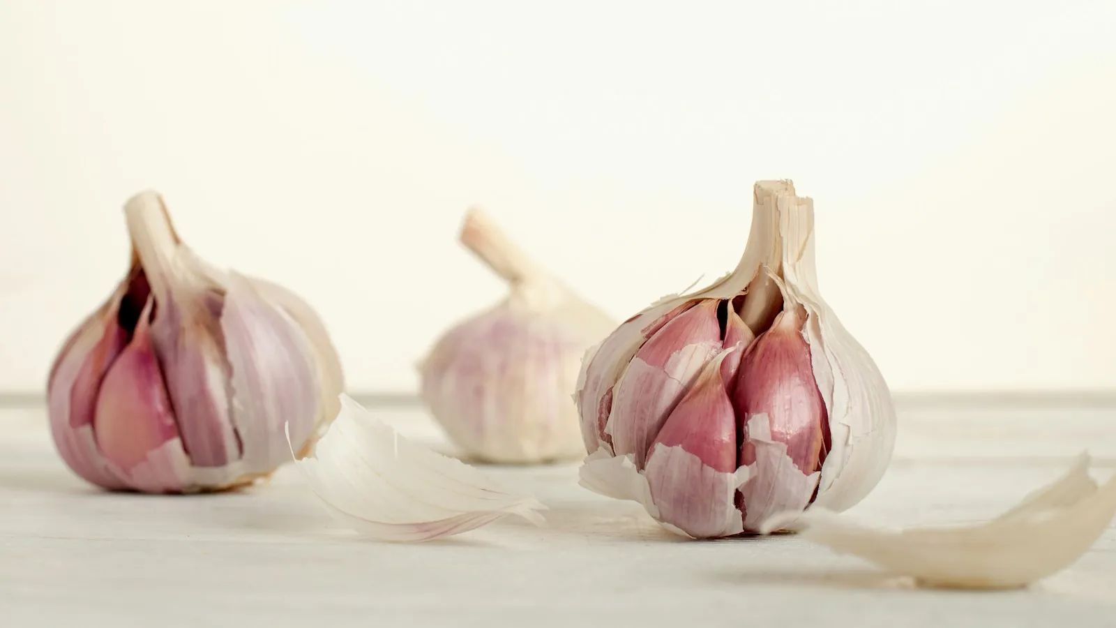 Three whole unpeeled garlic cloves sitting close together on a dark surface