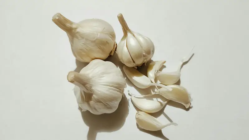 Three garlic bulbs and several loose cloves of different sizes on a white table
