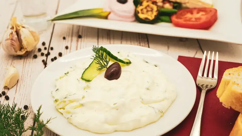 Creamy white yogurt dip topped with cucumber and dill on a plate with olives