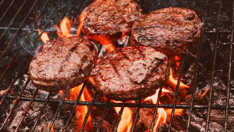 Burger patties searing over the black grate of a charcoal grill