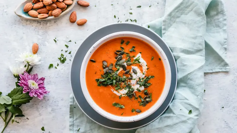 Bowl of smooth orange pureed soup on a styled table with garnish