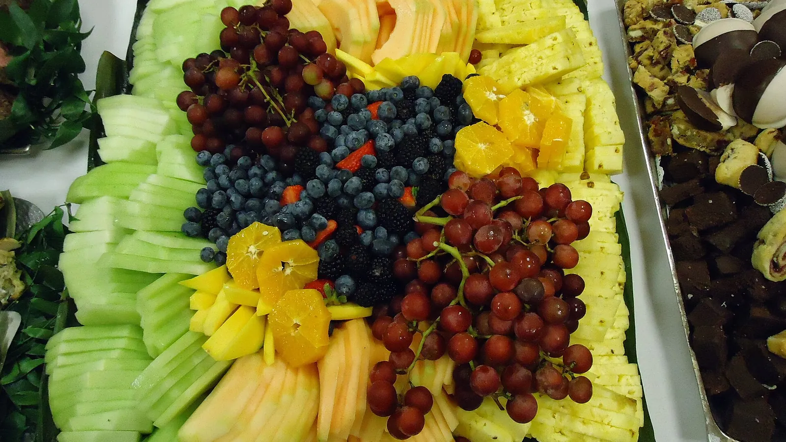 Fruit tray with pale green honeydew slices, cantaloupe, pineapple, grapes and berries