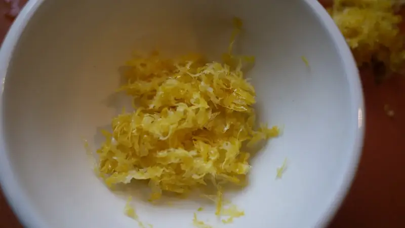 Fresh lemon zest piled in a small white bowl on a cutting board