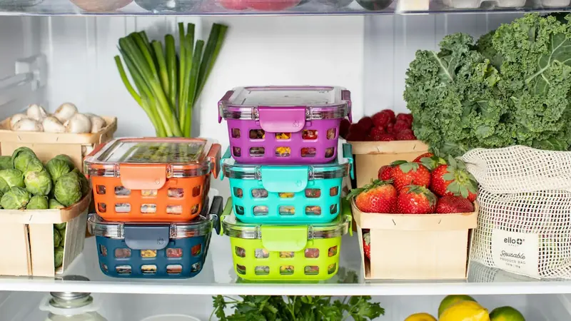 Stacked colorful food storage containers with leftovers on a refrigerator shelf