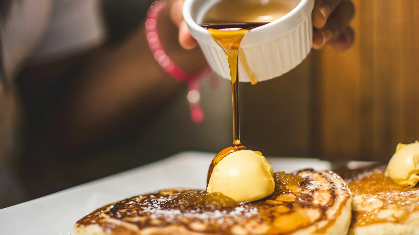 Maple syrup being poured over a stack of pancakes