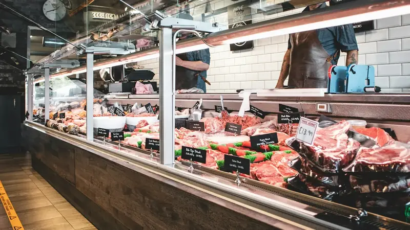 Raw cuts of meat lined up in a butcher's display counter, ready to be bought by the pound