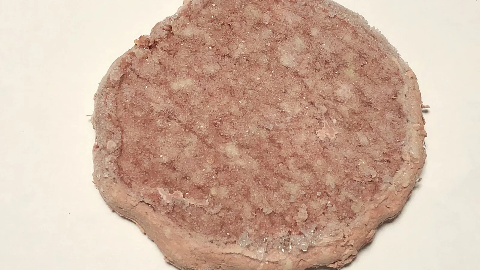 A frozen raw quarter pound ground beef patty on a plate