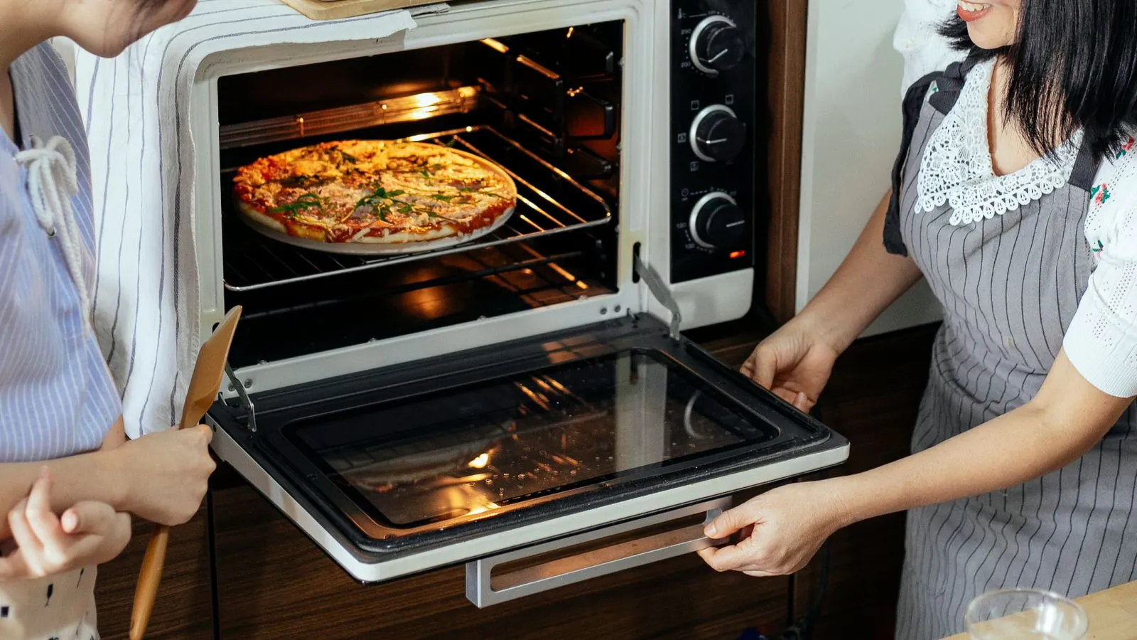 Two cooks sliding a homemade pizza into a hot electric oven