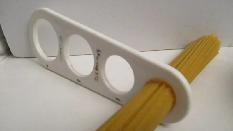One portion of dry spaghetti held in a spaghetti measure with holes for each serving