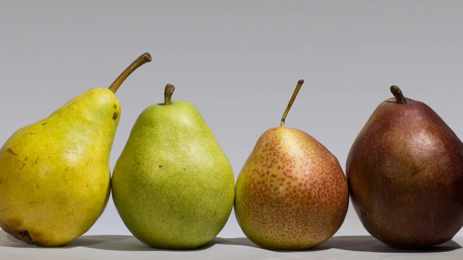 Four pears in a row, from yellow and green to speckled red and deep red