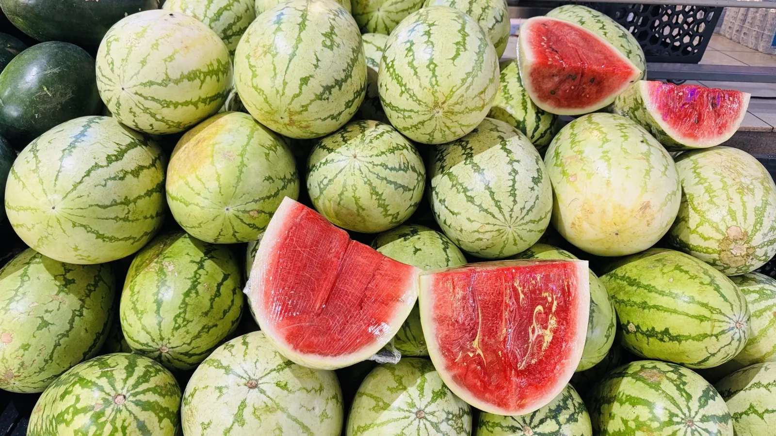 Pile of striped watermelons at a store with a few cut open to show red flesh