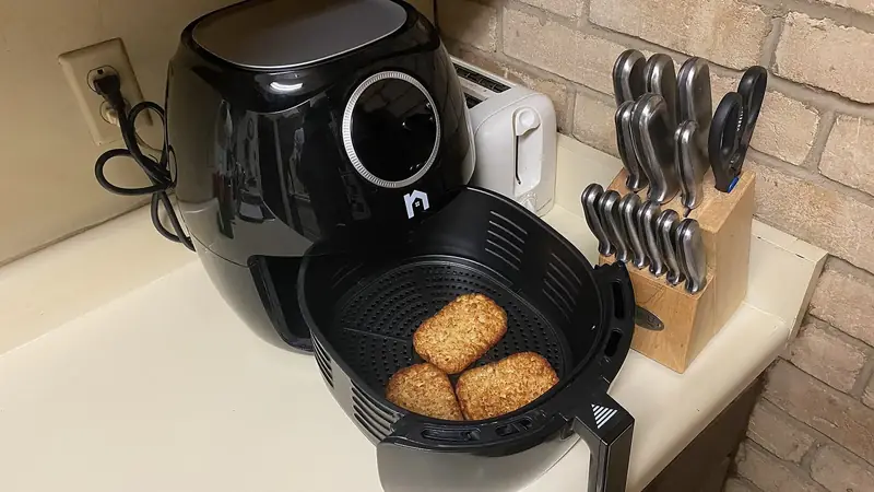 A countertop basket air fryer on a kitchen counter, used for cooking frozen hash brown patties