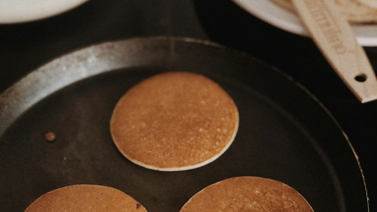 Small golden pancakes cooking in a black frying pan