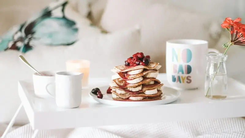 Pancakes topped with raspberries on a plate beside coffee mugs