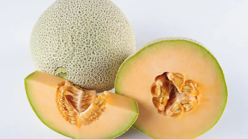 Whole ripe cantaloupe with tan netting beside two cut halves showing orange flesh and seeds