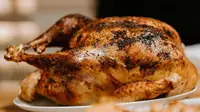 Golden brown roast whole chicken with crisp skin resting on a white ceramic plate
