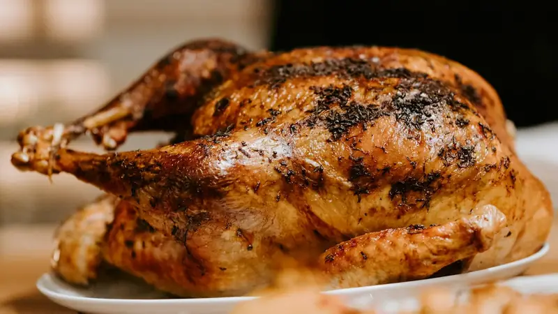 Golden brown roast whole chicken with crisp skin resting on a white ceramic plate