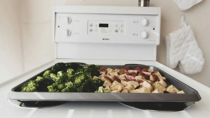 Seasoned broccoli florets and potato chunks spread on a gray sheet pan before roasting