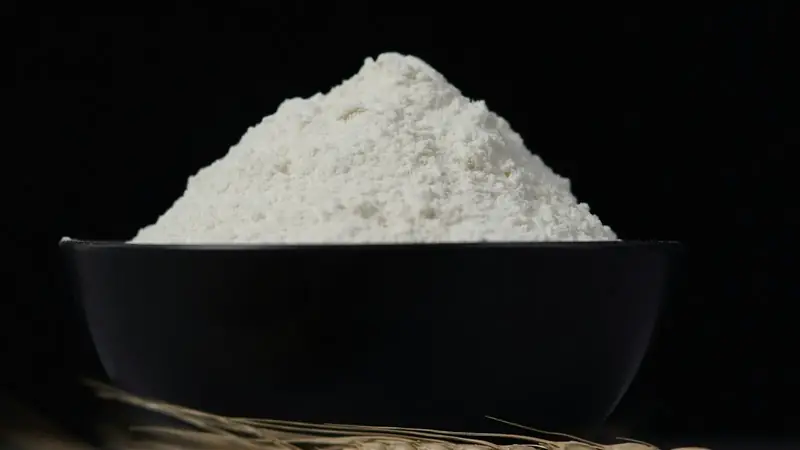 A bowl of white all purpose flour sitting on a kitchen table