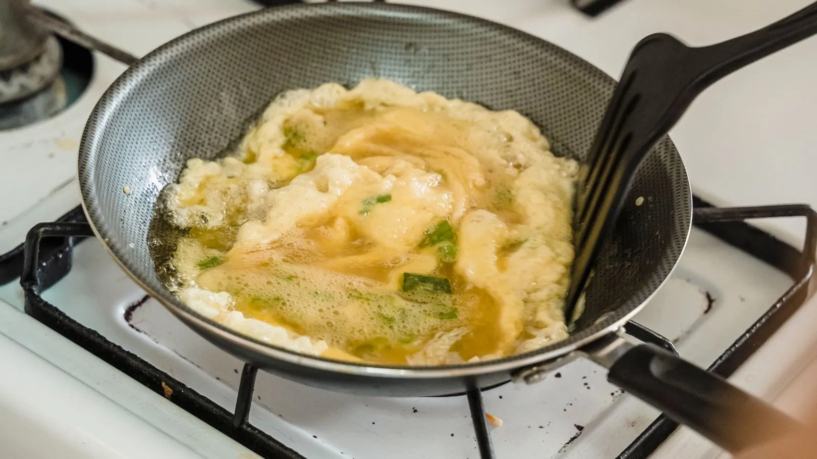 Scrambled eggs cooking in a frying pan on a gas stove with a spatula