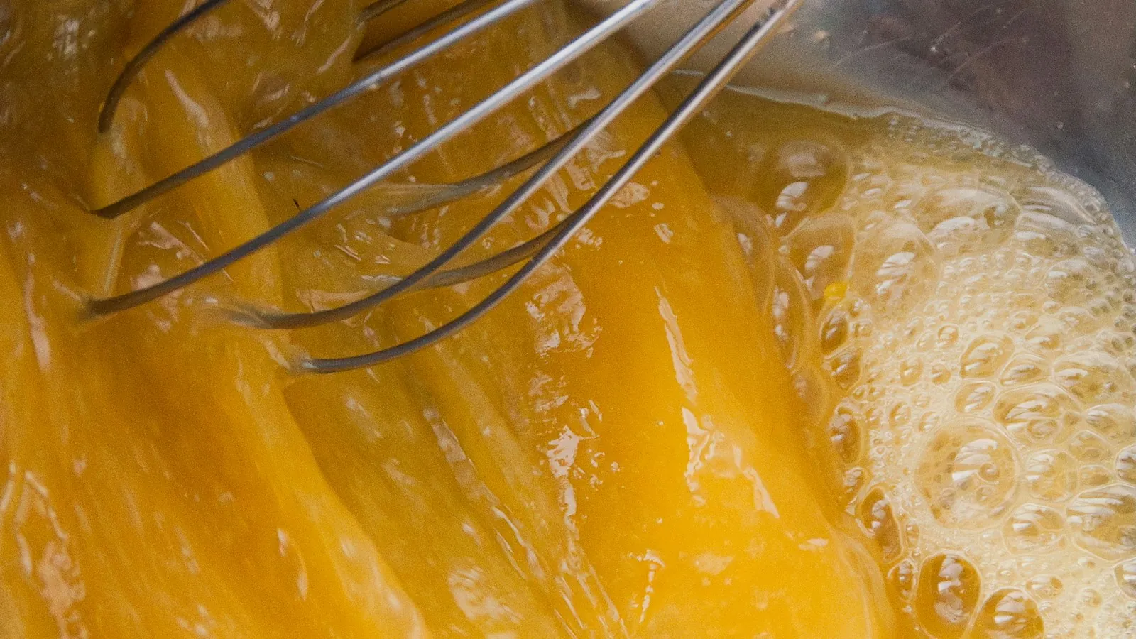 Whisking raw eggs in a metal bowl with a wire whisk