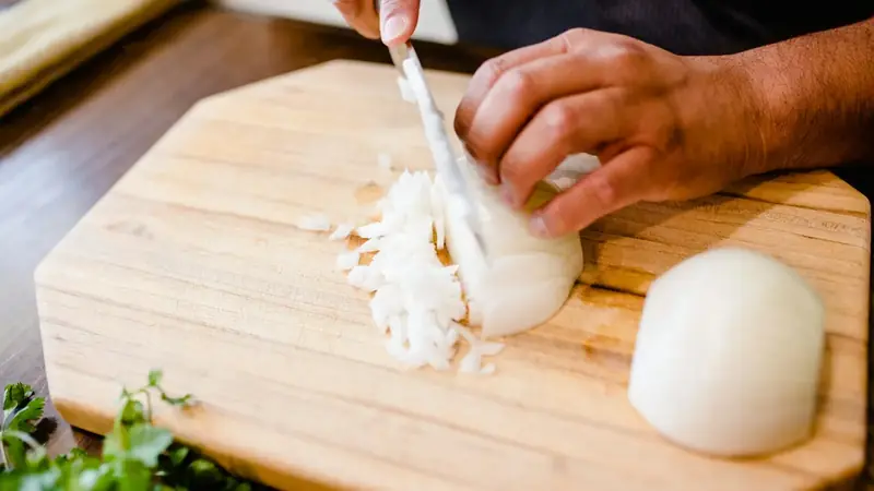 Person chopping a peeled onion on a wooden cutting board with a chef's knife
