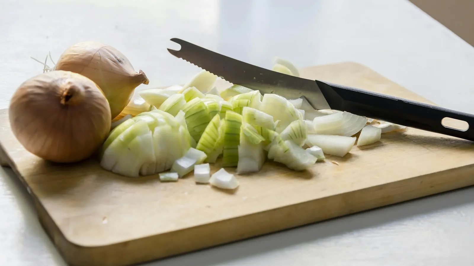 Cutting board with whole onions and a knife ready for prep