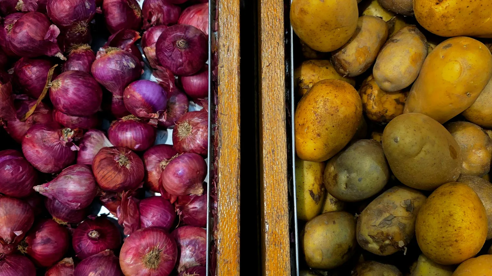 Red onions and potatoes sitting in separate wooden bins