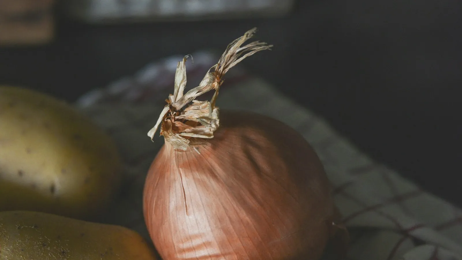 Brown potatoes and a brown onion side by side on a plain surface